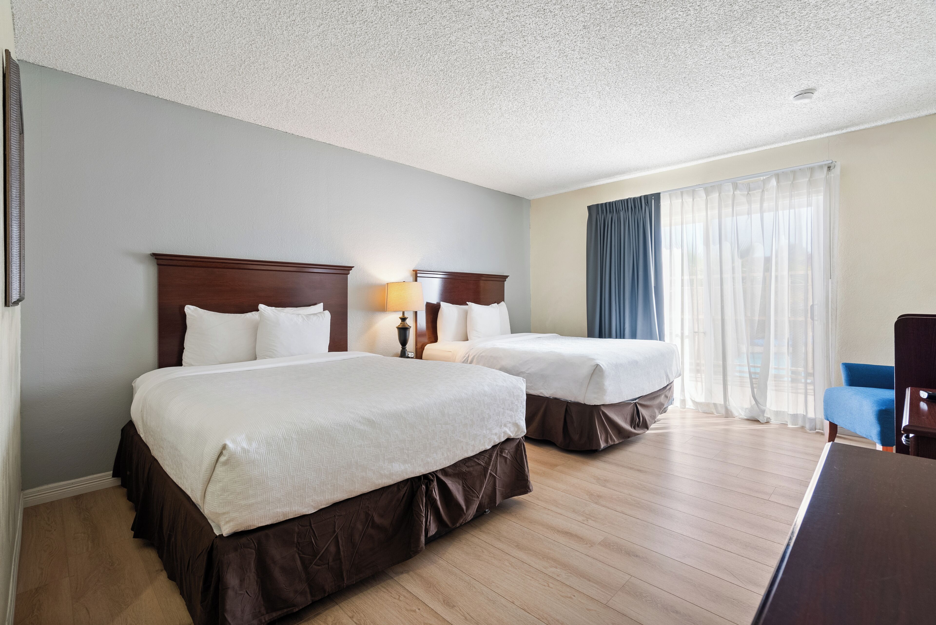 A hotel room with two beds, a desk, a chair, and a window with curtains.