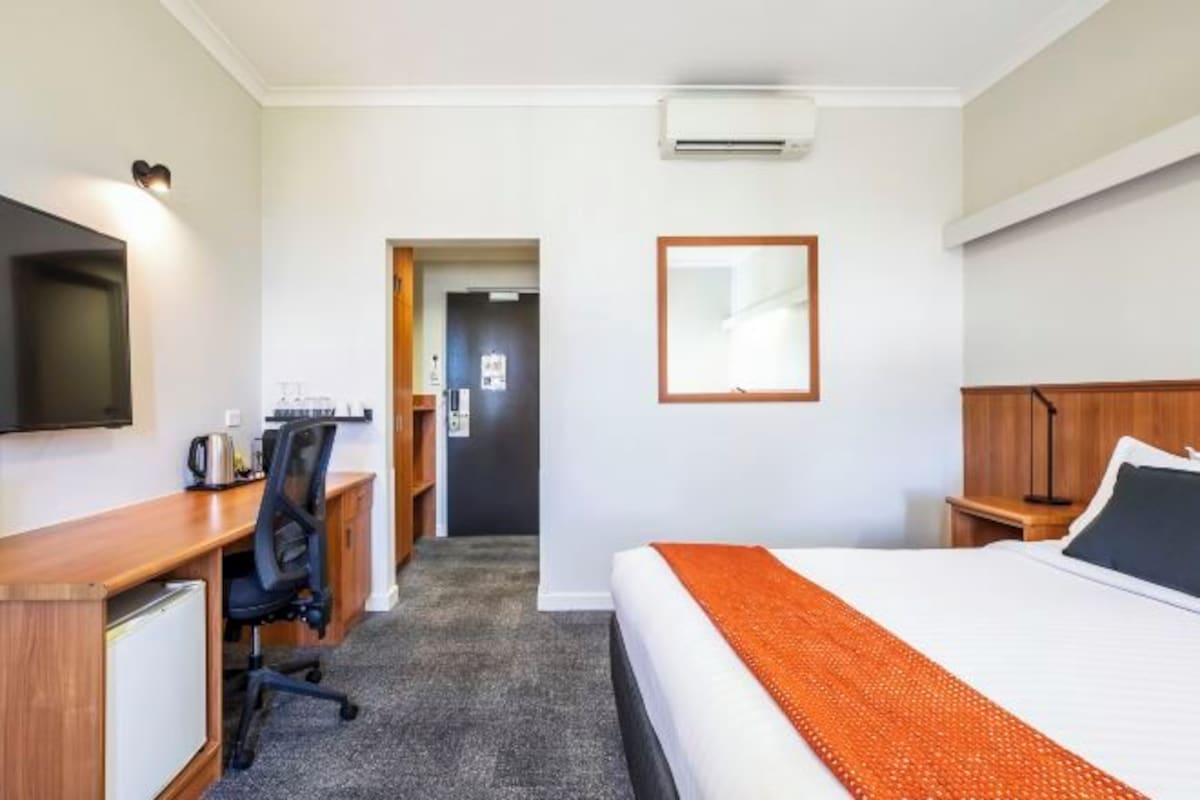 Habitación de hotel con cama, escritorio, silla y televisor.