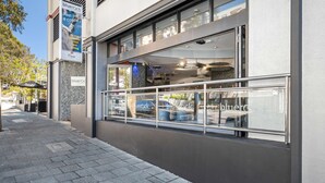 A modern building with a glass facade, a metal railing along the sidewalk, and a sign advertising a restaurant. - Metro Hotel Perth City (East Perth)