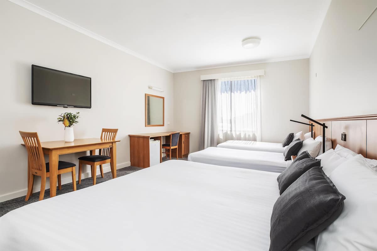 A hotel room with two beds, a desk with a chair, a television, and a window with curtains.