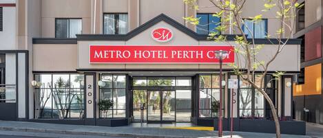 The exterior of the Metro Hotel Perth City with a modern facade, large glass entrance, and a prominent hotel sign.