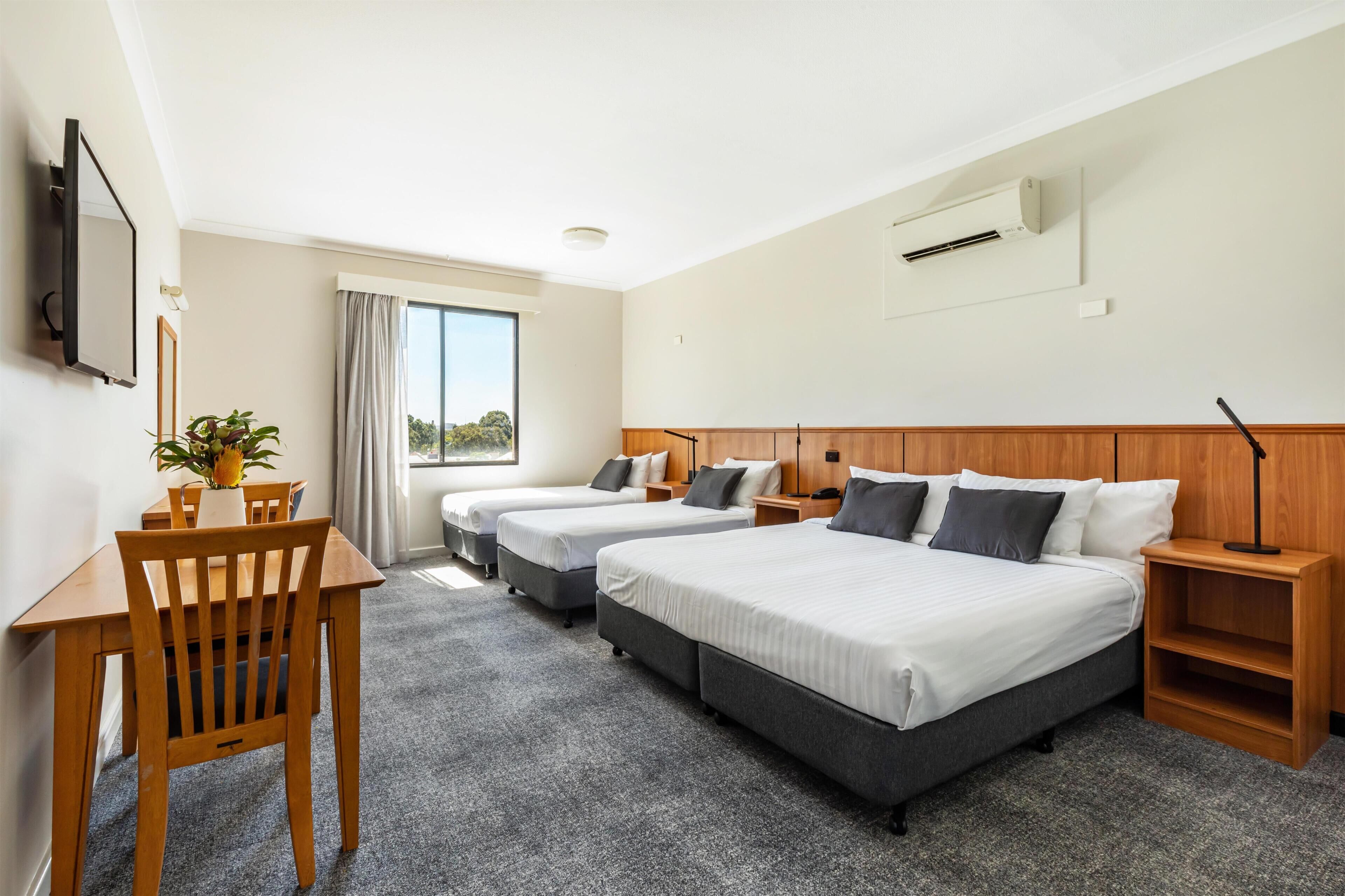 A hotel room with two beds, a desk, a chair, a TV, and a window.