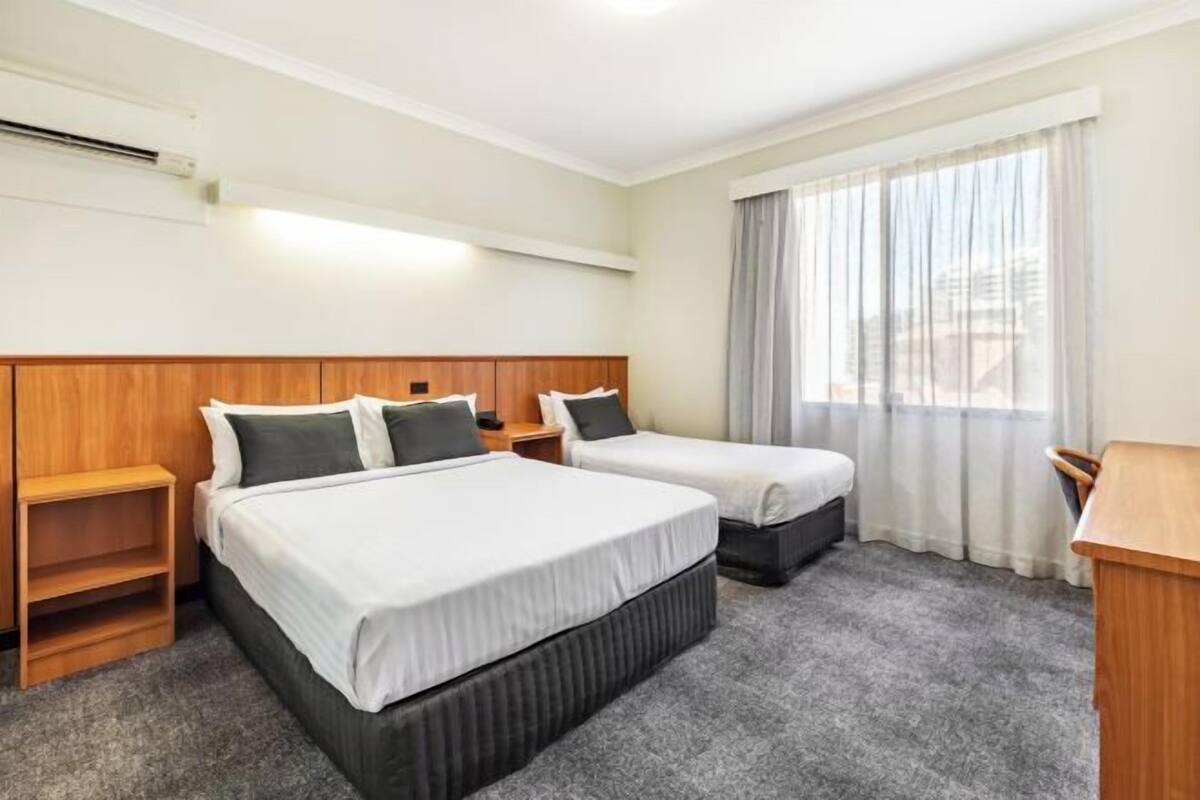 A hotel room with two beds, a desk, a chair, and a window with curtains.