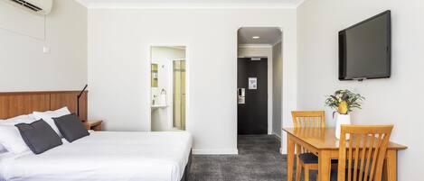 A hotel room with a bed, bedside table, TV, and a dining area with chairs and a table.