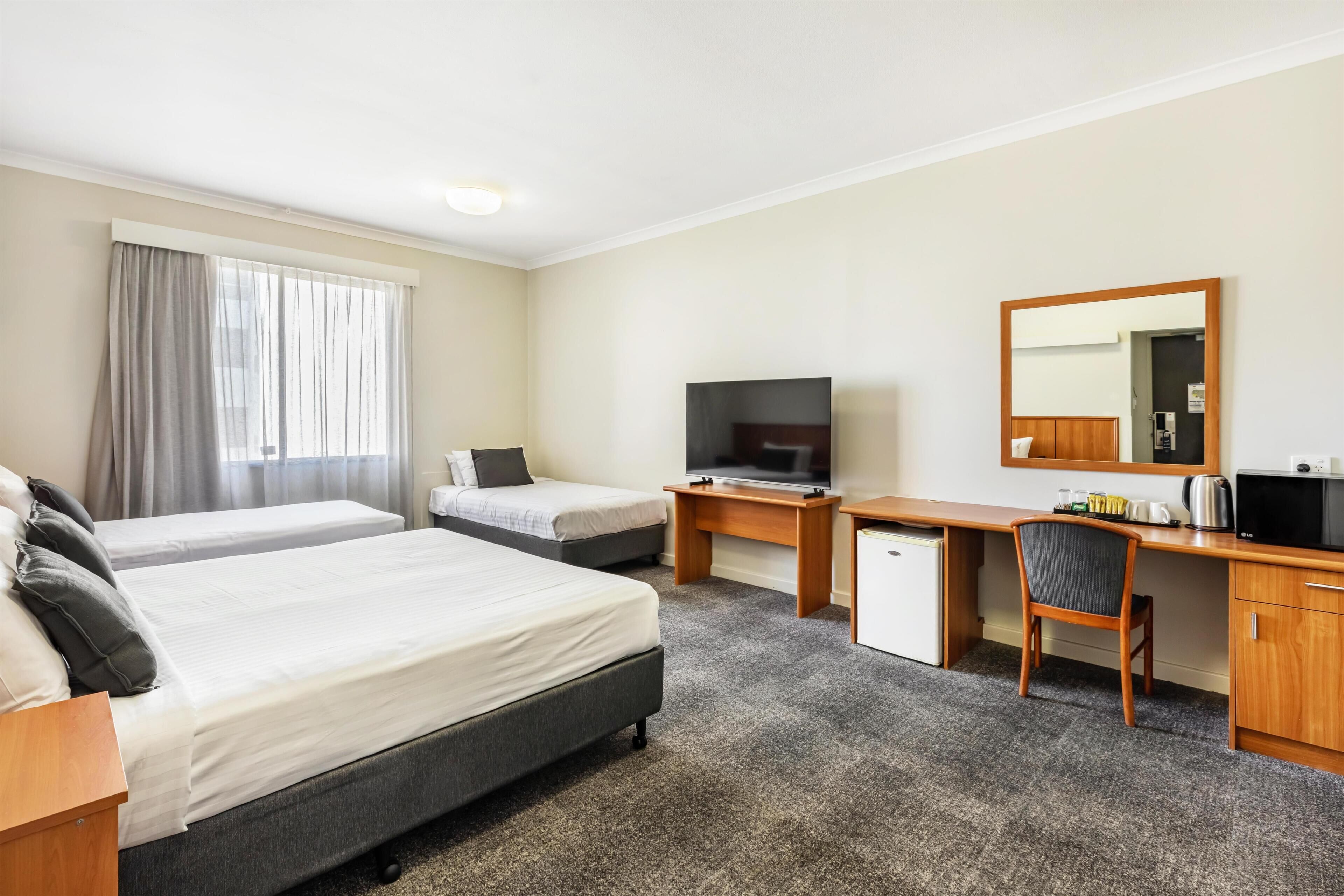 A hotel room with two beds, a desk with a TV, a small refrigerator, and a mirror.