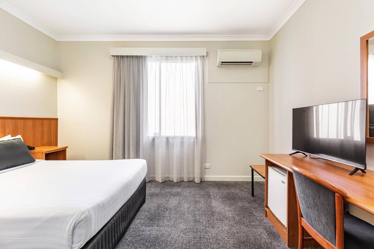 A hotel room with a bed, a desk, a television, an air conditioner, and a window with curtains.