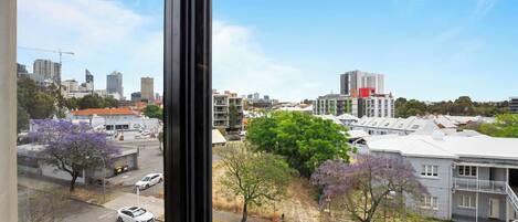 A cityscape with modern buildings, a parking area, and trees with purple flowers.