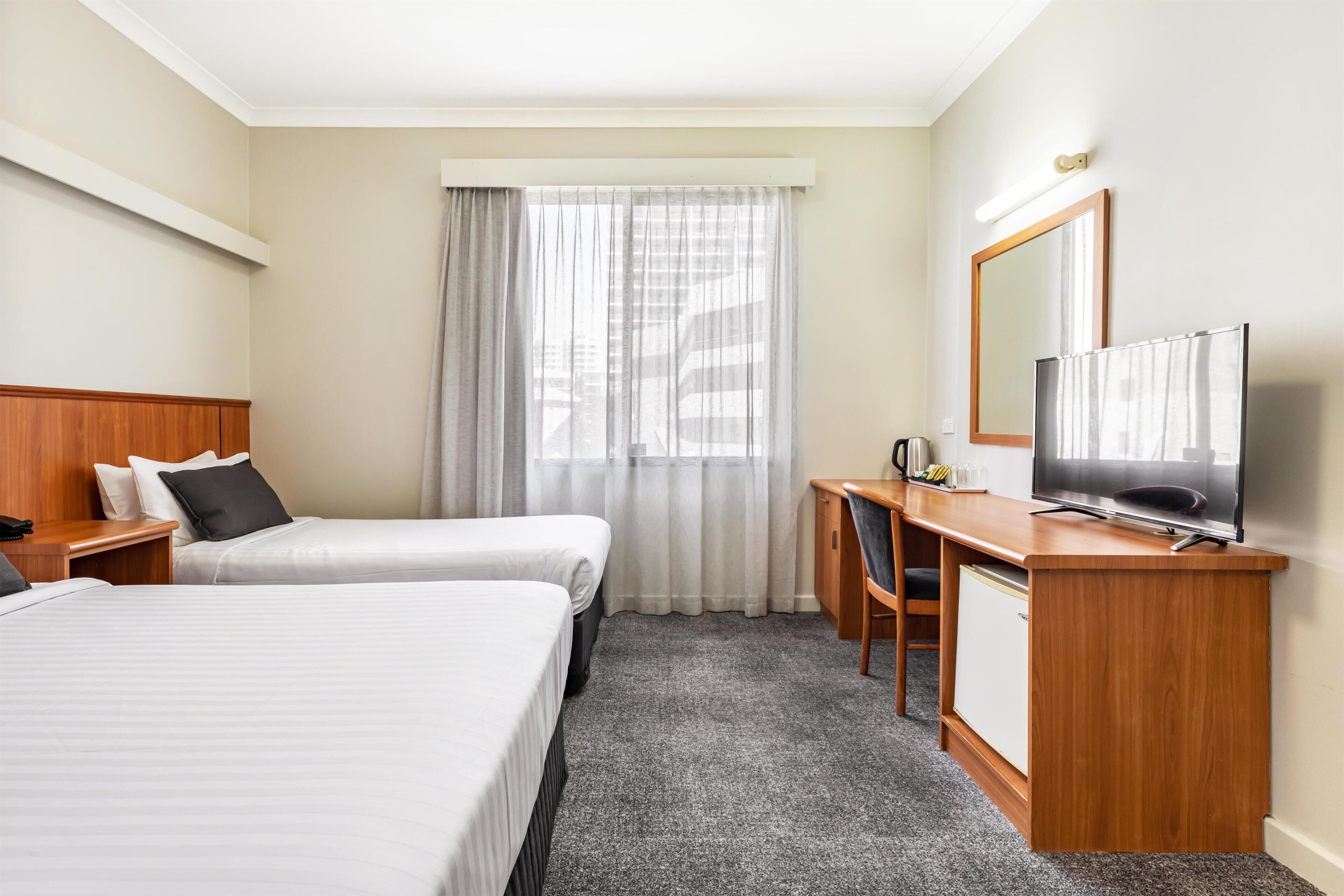 A hotel room with two beds, a desk with a TV, a chair, and a window with curtains.