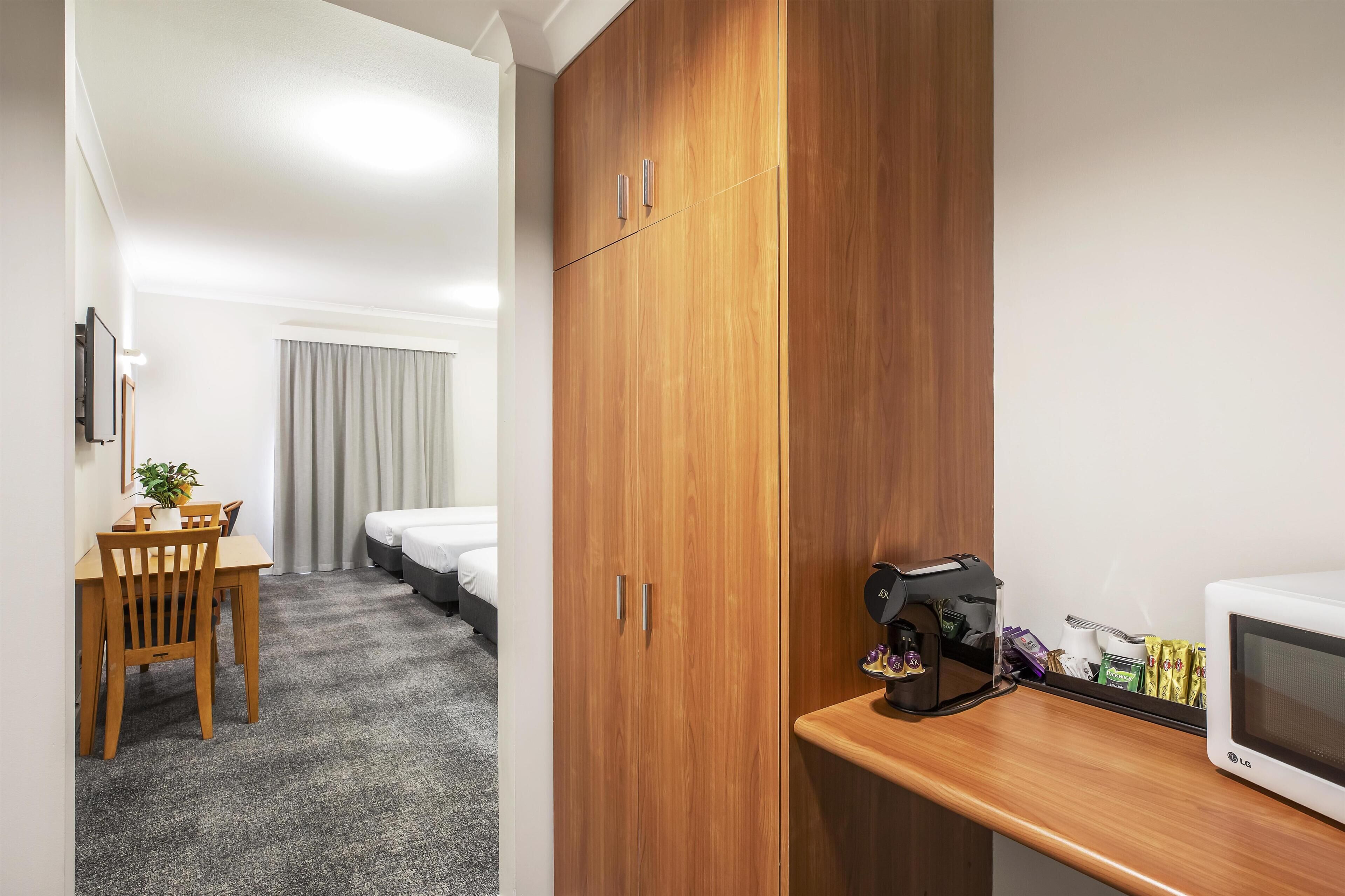 Une chambre d’hôtel équipée d’une armoire en bois, d’une table à manger avec des chaises, d’un lit, d’un four à micro-ondes et d’une machine à café.