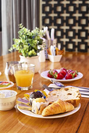 A breakfast table with croissants, strawberries, a glass of orange juice, and a bowl of yogurt.