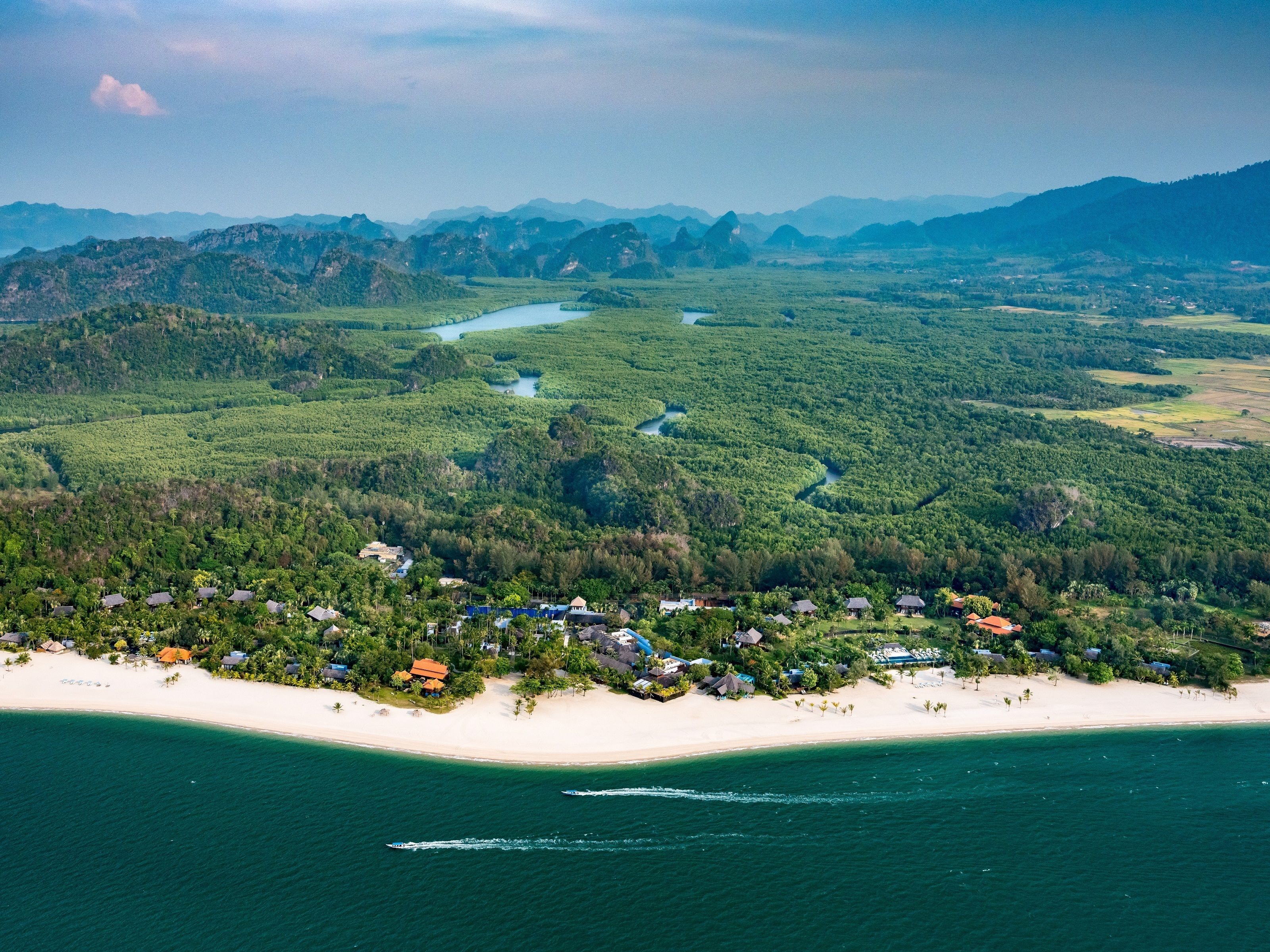 An aerial view of a coastal area with a beach, a river, and a forested landscape.
