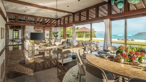 Amplia sala de estar con un gran ventanal con vistas a la playa, amoblada con un sofá, una mesa de comedor y sillas.