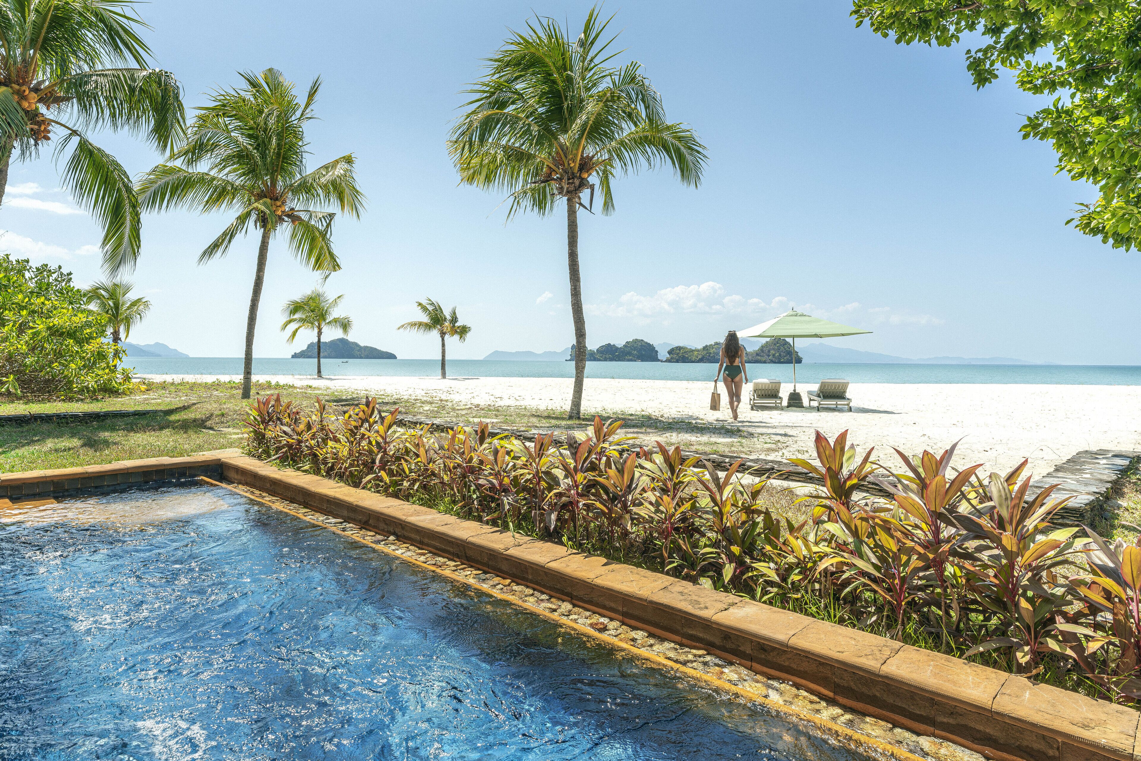 A swimming pool with a view of a beach and palm trees.
