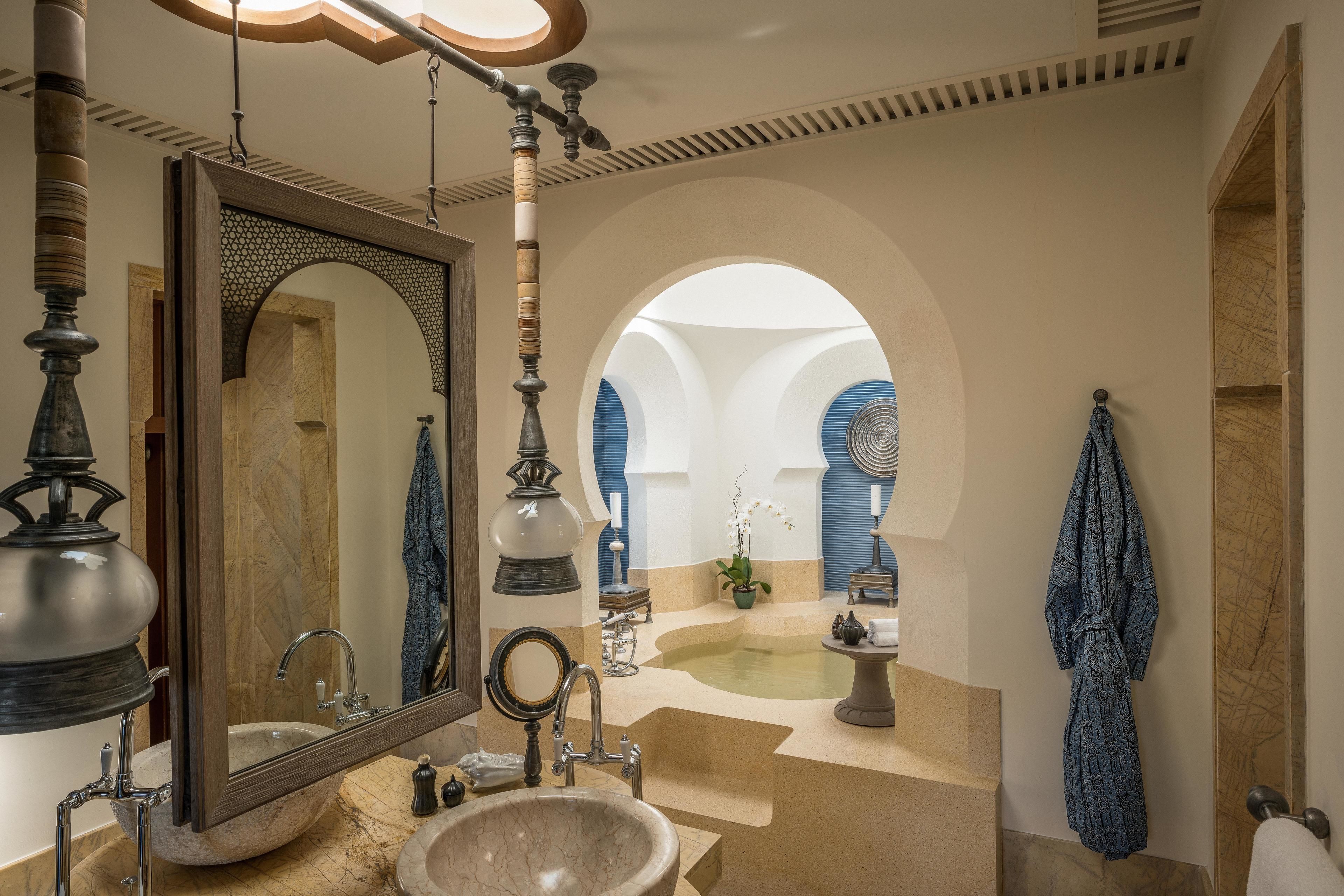 A luxurious bathroom with a large mirror, a marble sink, a bathtub, and a small table with a plant.