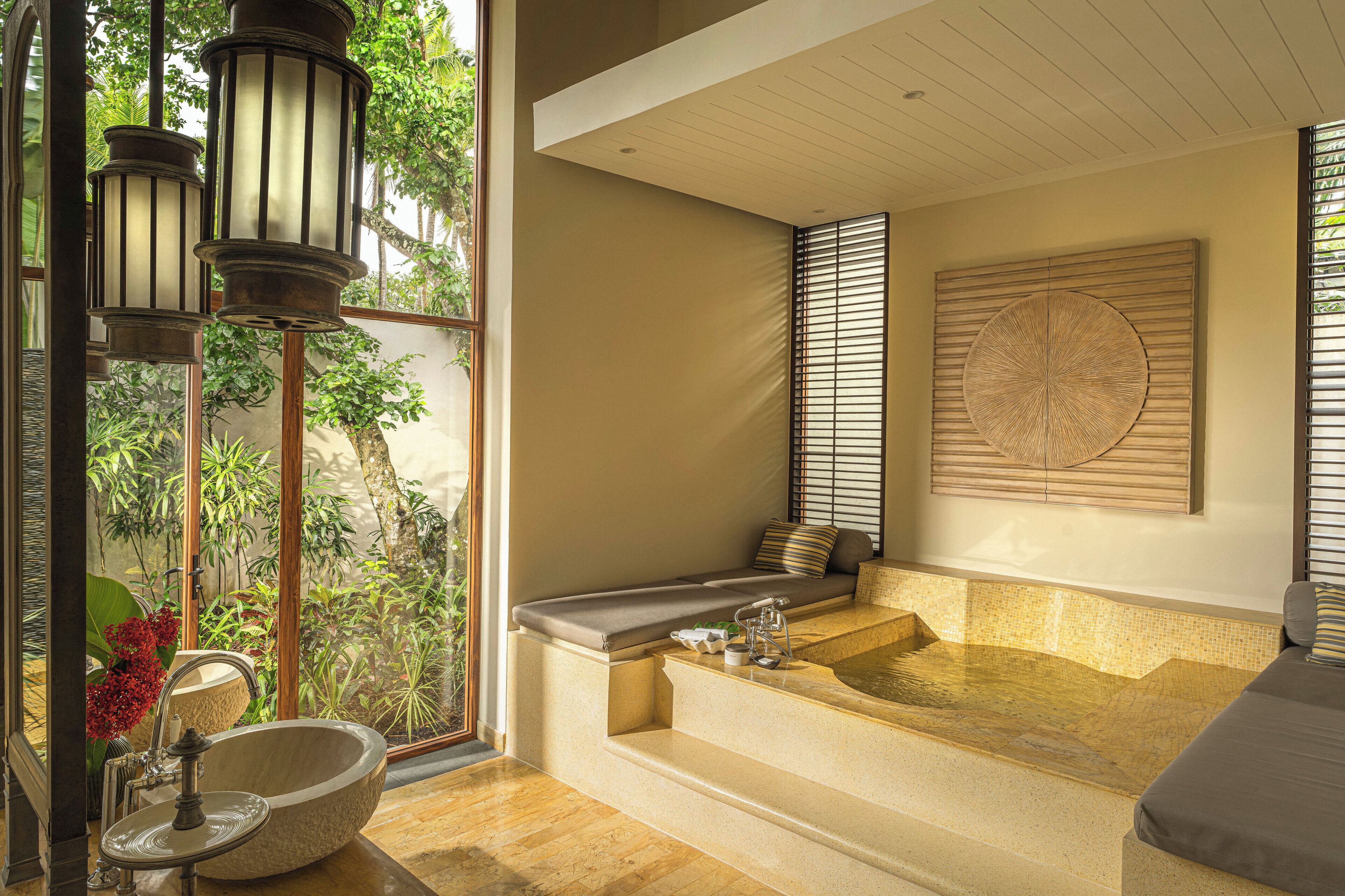 Un cuarto de spa con una bañera grande, una ventana con vista a follaje y un diseño circular montado en la pared.