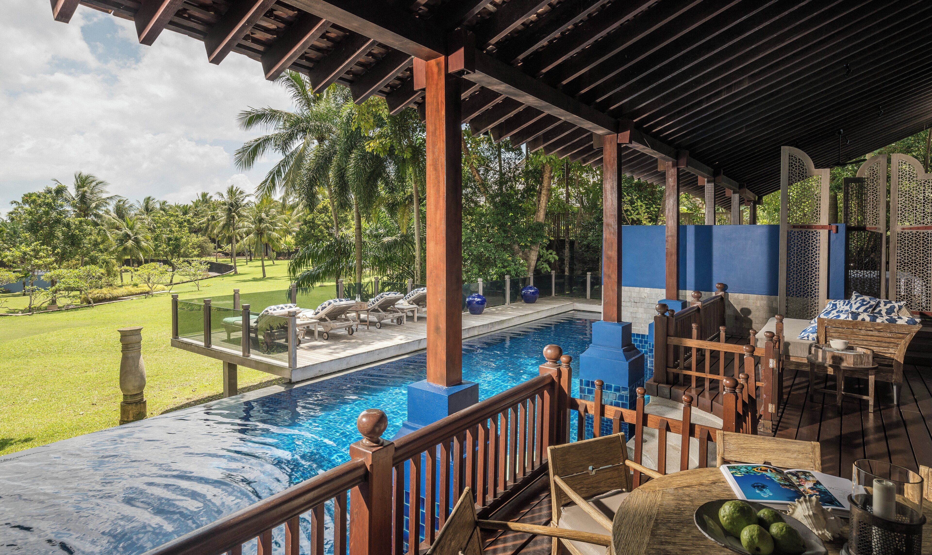 A poolside area with lounge chairs, a wooden deck, and a view of a lush garden.