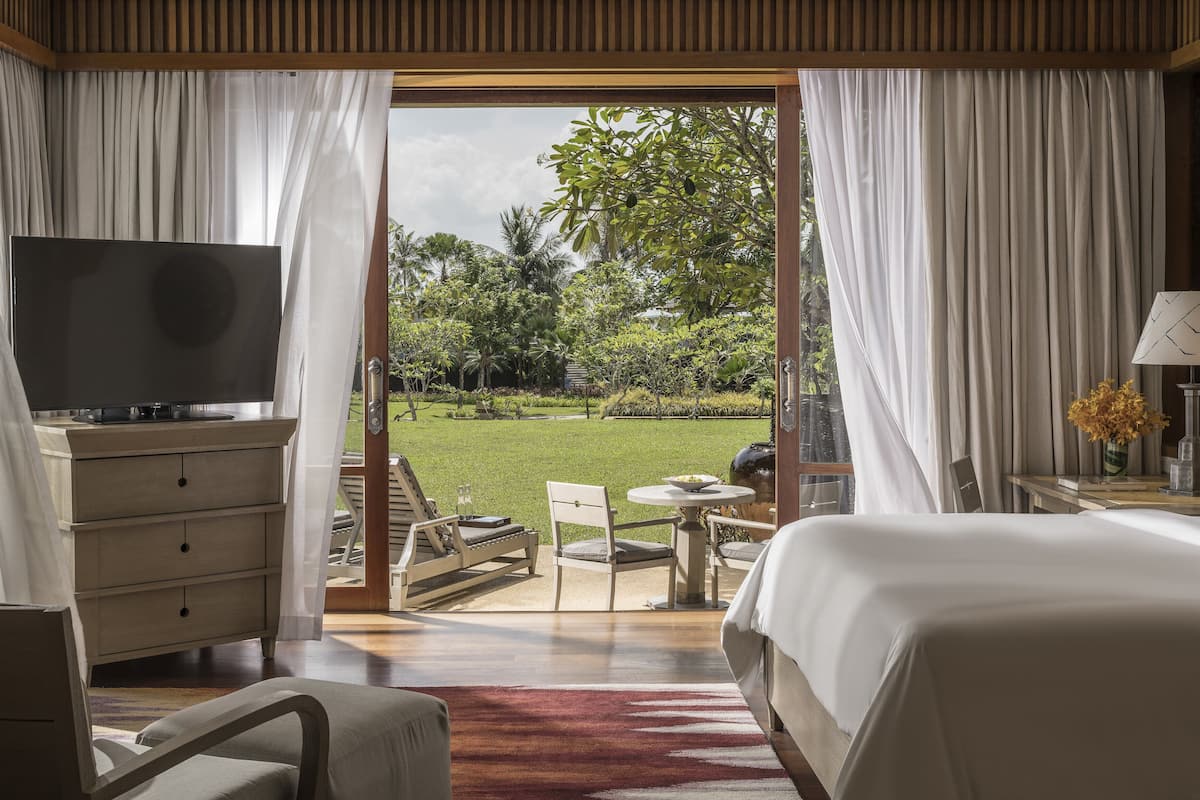 Un dormitorio con televisor, cama, escritorio y vistas a un jardín.