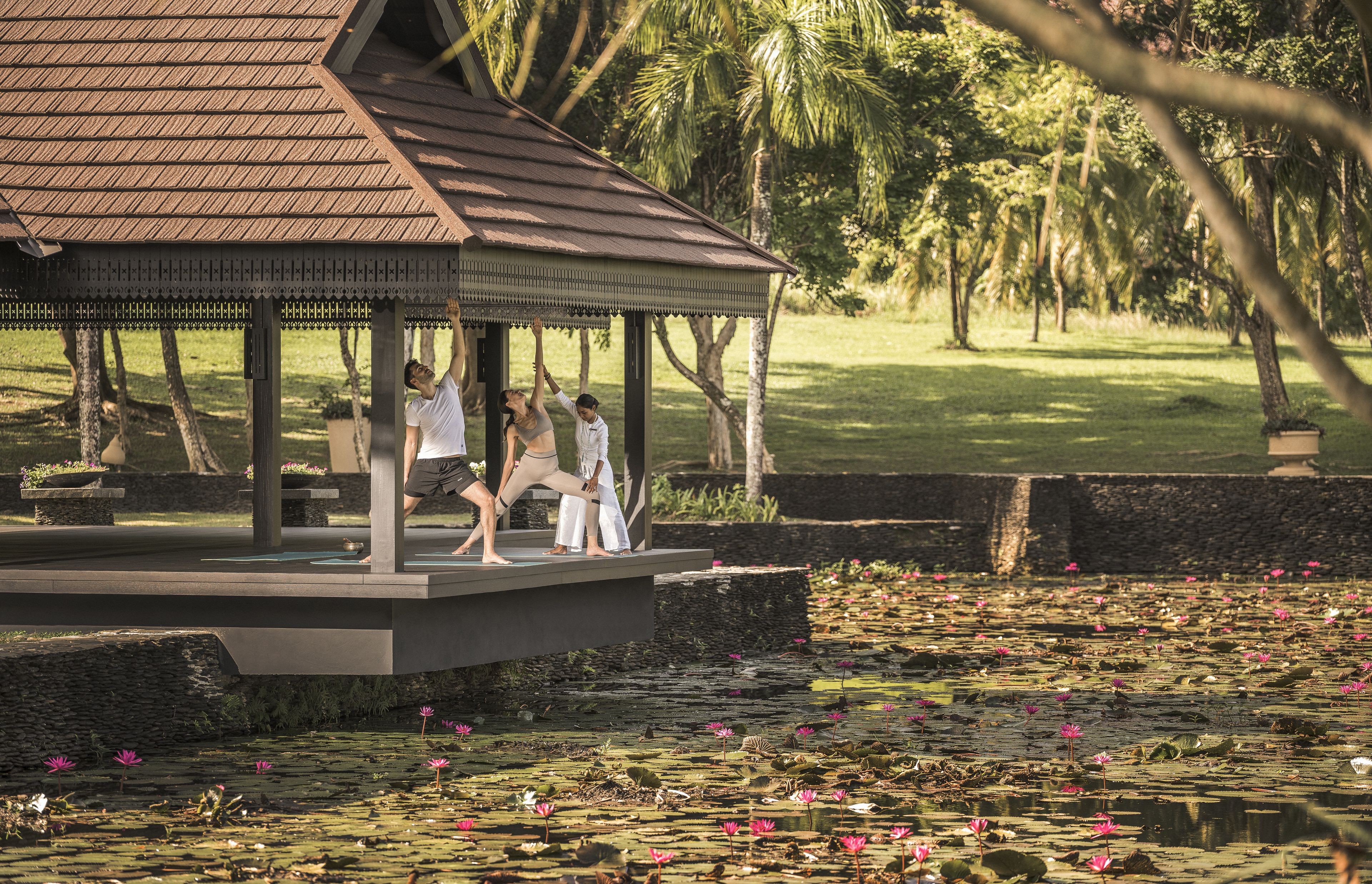 A gazebo with a tiled roof and a stone base, surrounded by a pond with lotus flowers.