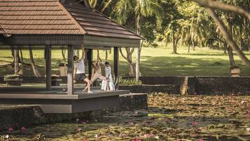 A gazebo with a tiled roof and a stone base, surrounded by a pond with lotus flowers.