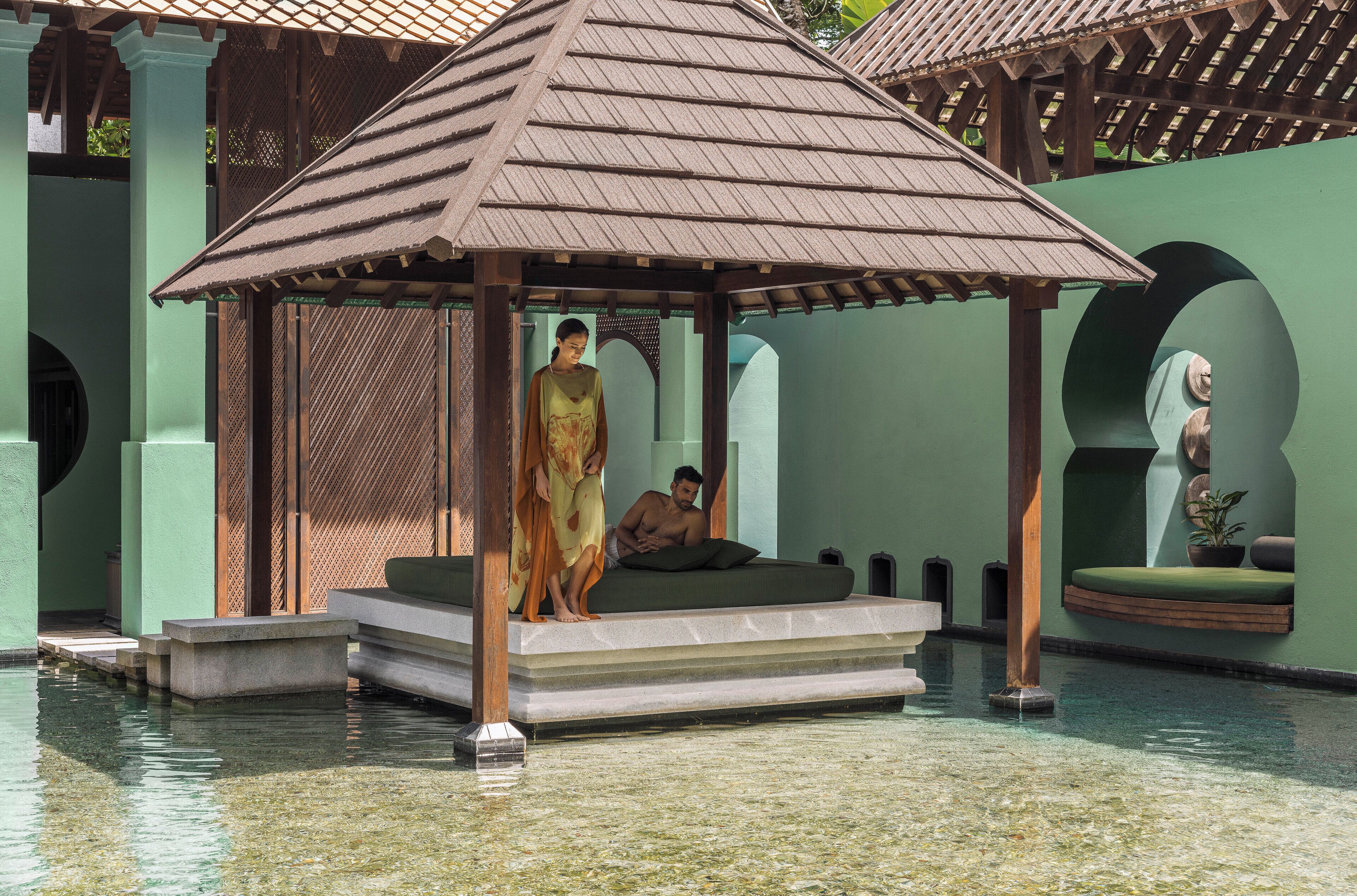 A traditional pavilion with a tiled roof, a stone platform, and a pool in the foreground.
