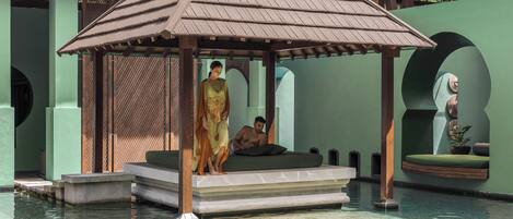 A traditional pavilion with a tiled roof, a stone platform, and a pool in the foreground.