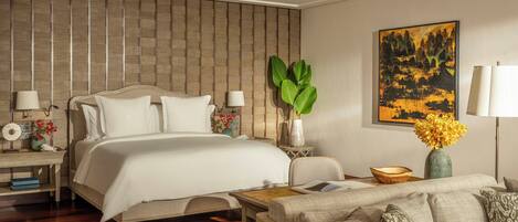 A modern hotel room with a large bed, a sofa, a coffee table, and a wall-mounted painting.