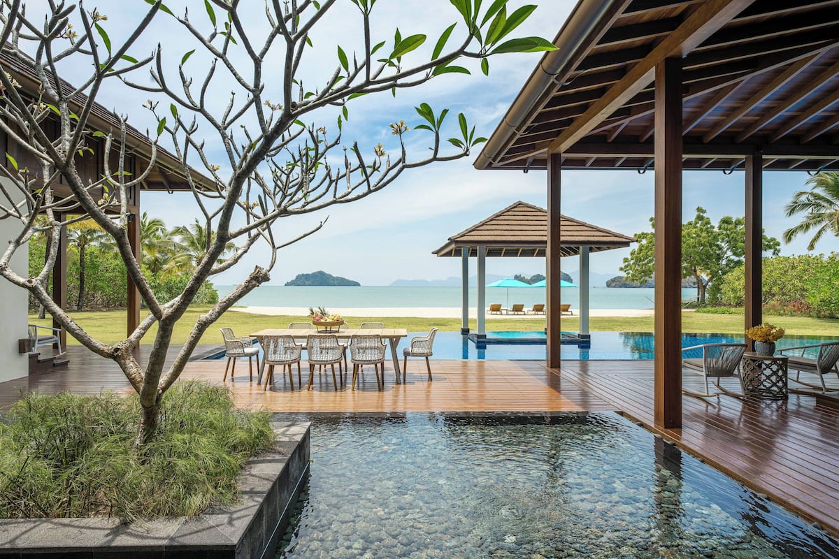 Una terraza de madera con piscina, mobiliario exterior y vistas al mar.