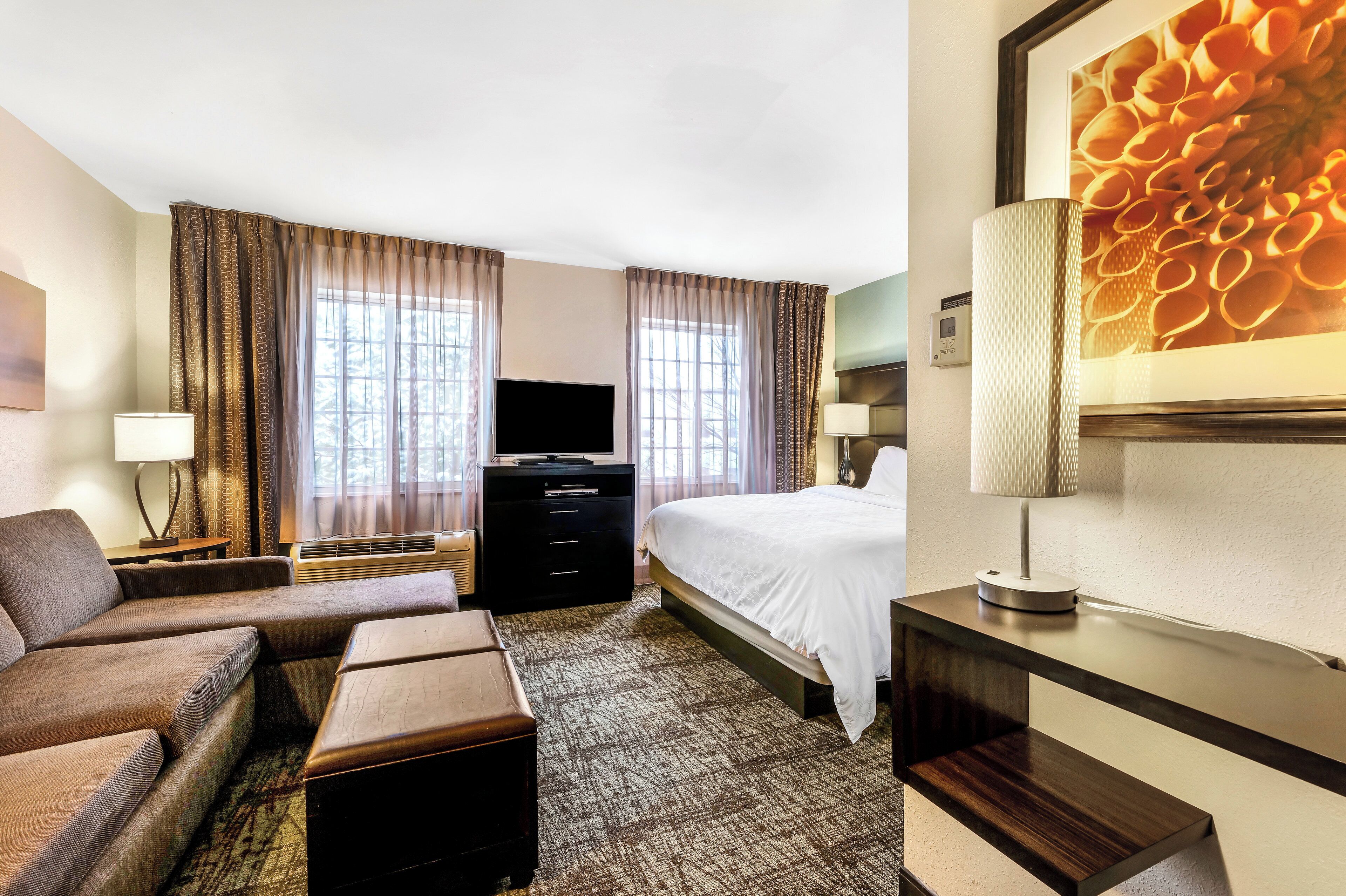 Une chambre d’hôtel avec un lit, un canapé, une télévision, un bureau et une grande fenêtre.