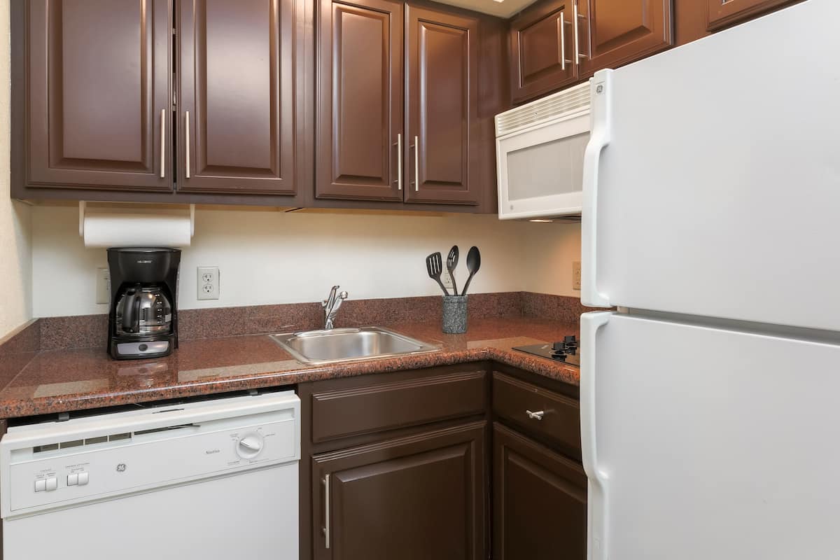 A kitchen with brown cabinets, a white dishwasher, a white refrigerator, a microwave, and a coffee maker.