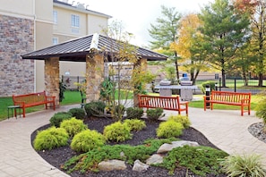 A covered outdoor seating area with benches, surrounded by landscaped garden beds and trees. - Staybridge Suites Philadelphia-Mt. Laurel by IHG (Mount Laurel)