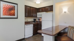 A compact kitchen with dark brown cabinets, a white dishwasher, a white refrigerator, and a granite countertop. - Staybridge Suites Philadelphia-Mt. Laurel by IHG (Mount Laurel)