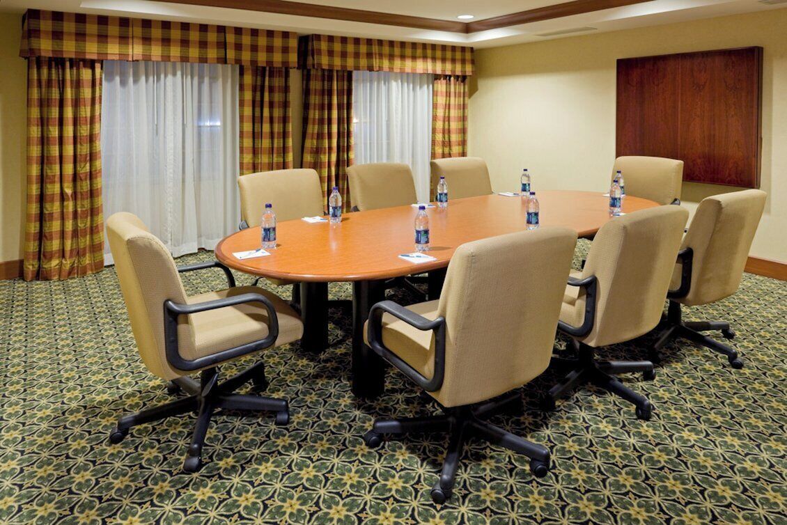 Un salón de conferencias con una mesa redonda, seis sillas y botellas de agua sobre la mesa.