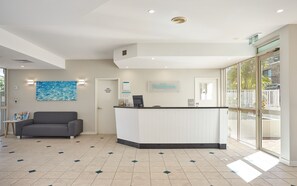 A reception area with a reception desk, a couch, a painting, a fire control room door, and a sign indicating the Maldives resort. - Maldives Resort (Main Beach)