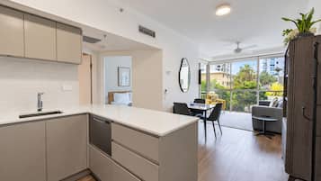 Una cocina moderna con una isla central, una zona de comedor con un sofá amarillo y vistas a un paisaje urbano a través de amplios ventanales.