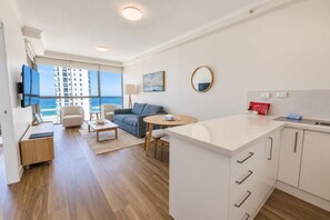 A modern hotel room with a kitchen, dining area, and a large window overlooking the ocean. - Maldives Resort (Main Beach)