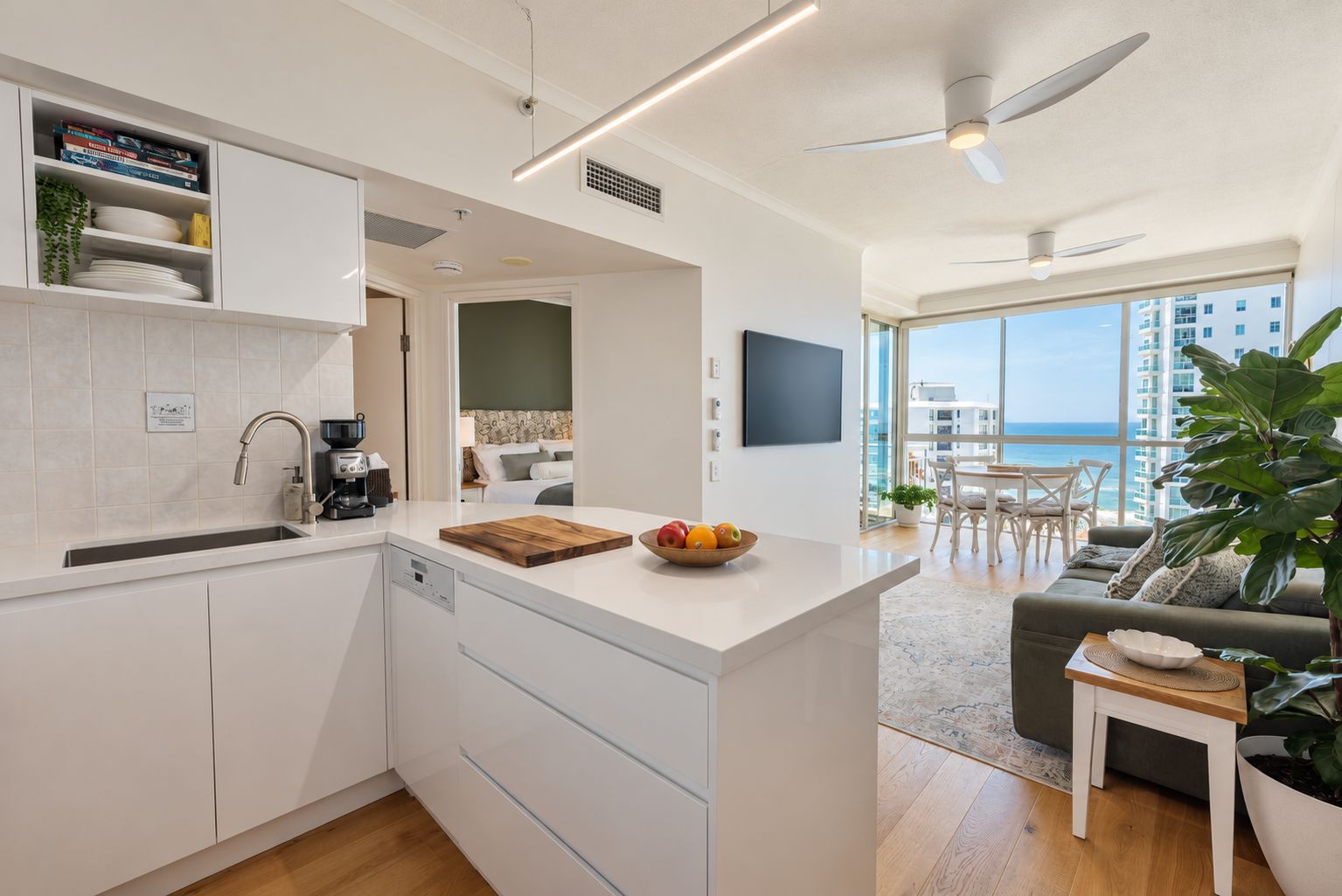 A modern kitchen with a central island, a dining area with a view, and a living room with a large plant.