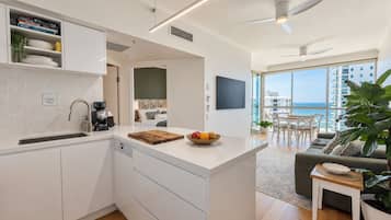 A modern kitchen with a central island, a dining area with a view, and a living room with a large plant.