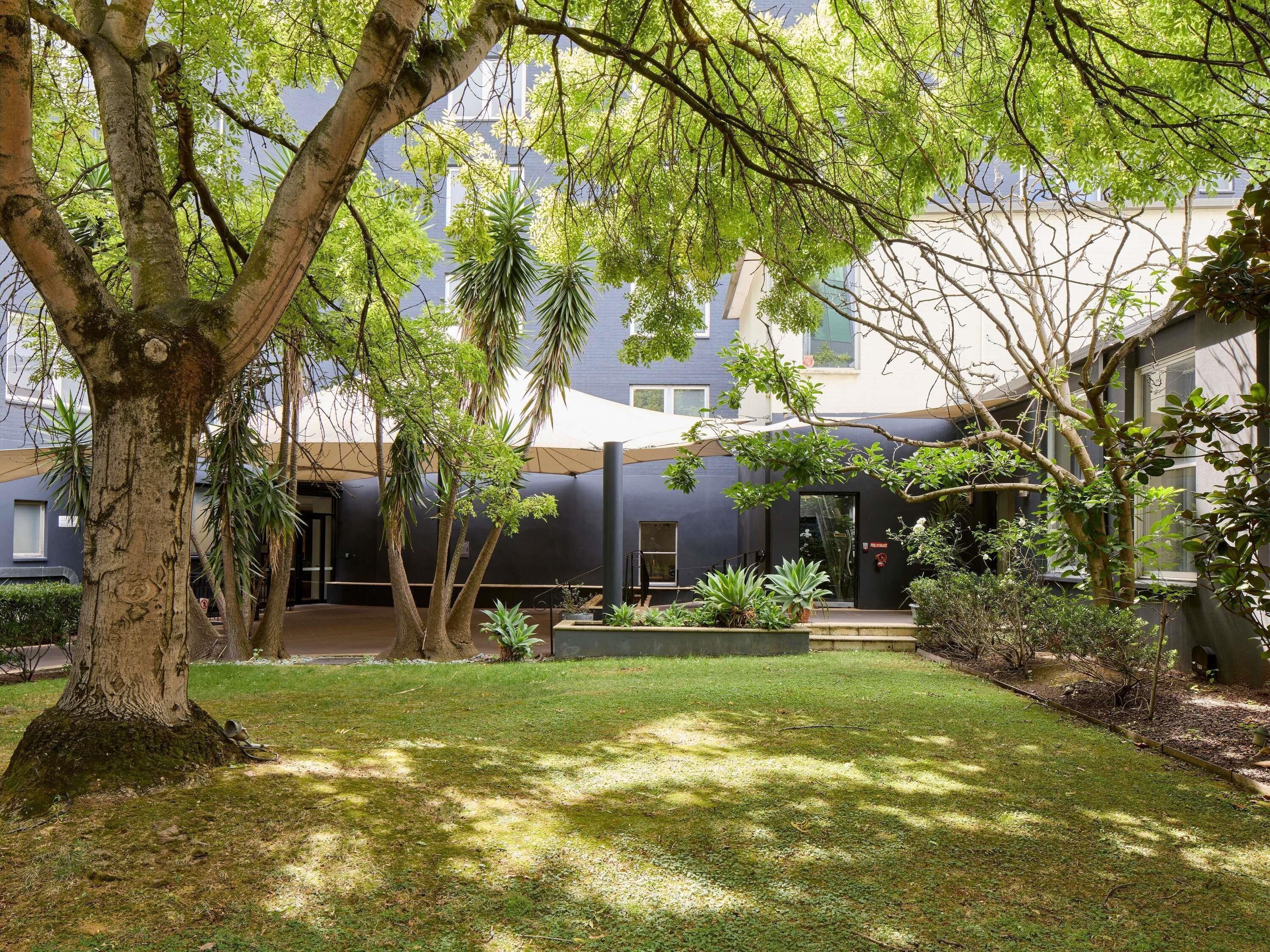 A courtyard with trees, a grassy area, and a building with a dark facade.