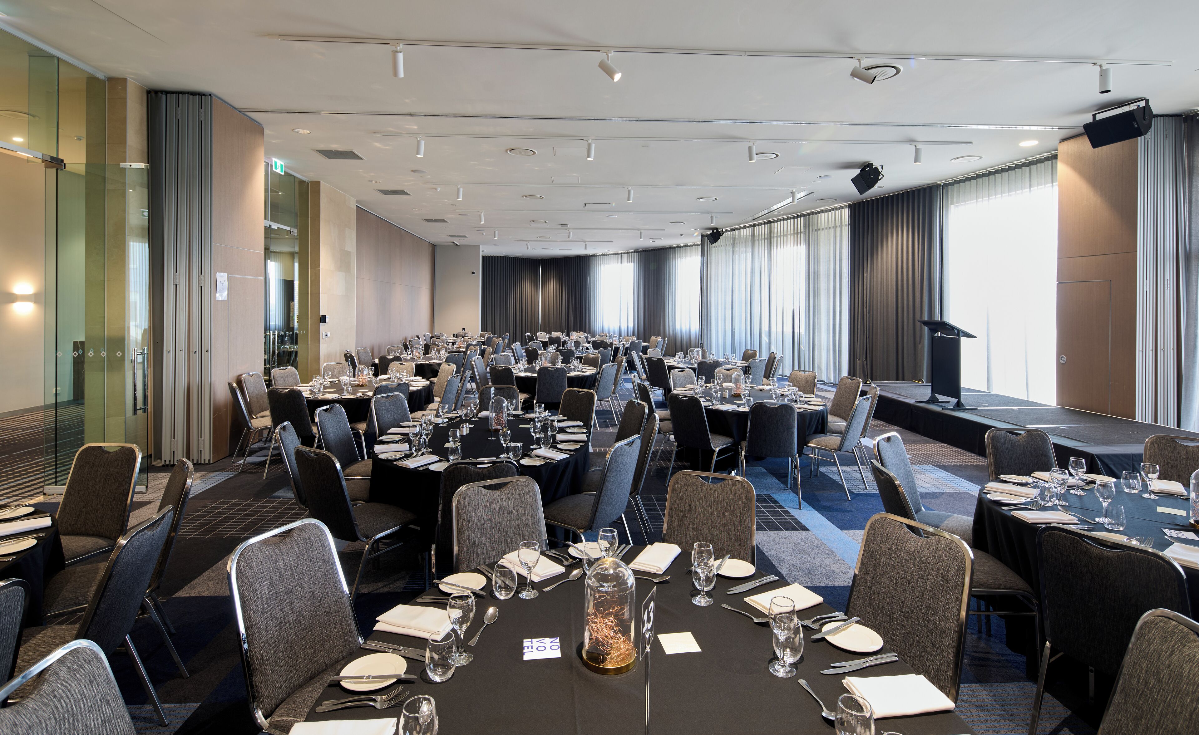 Une salle de conférence avec plusieurs tables disposées pour une réunion, équipée de chaises, de tables et d’une scène avec un pupitre.