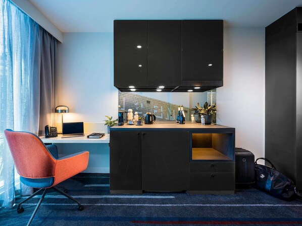 Ein kleines Hotelzimmer mit Schreibtisch, Stuhl, Küchenzeile und Blick auf die Stadt.