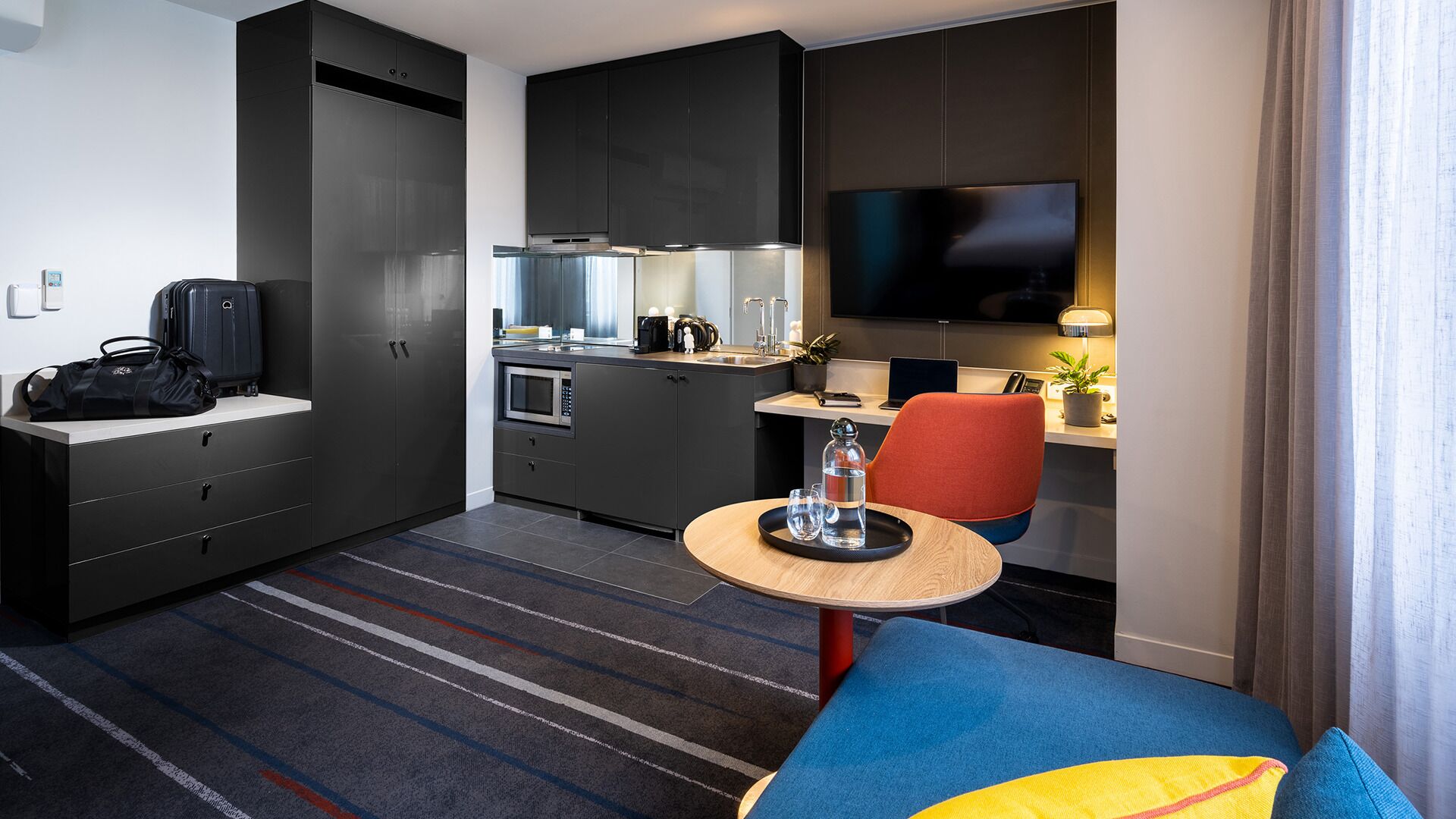 Habitación de hotel compacta con kitchenette, televisor, pequeña mesa de comedor y sofá.