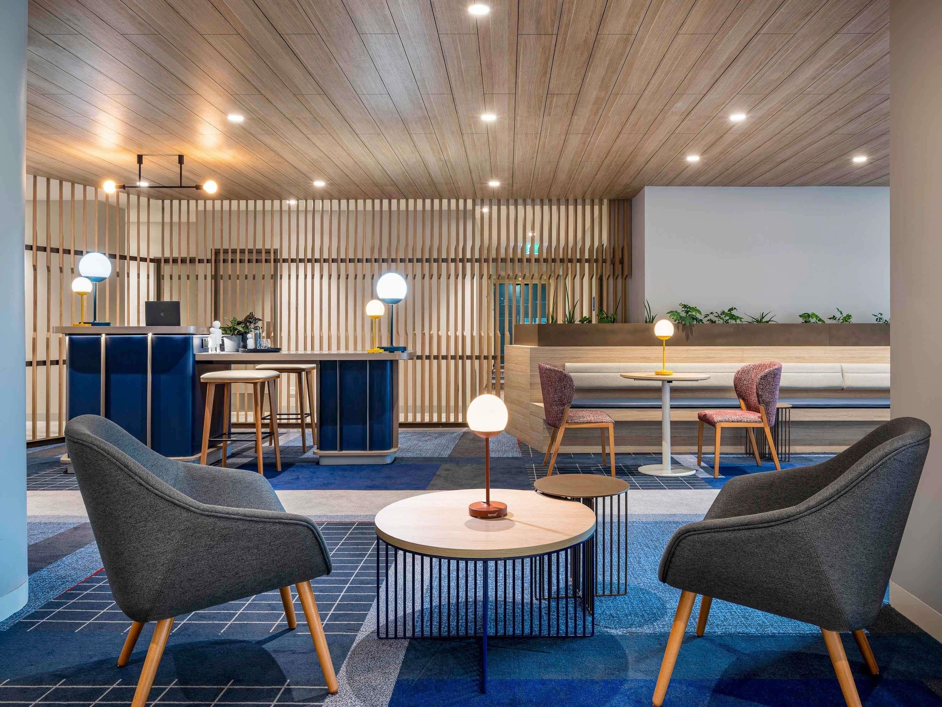 Un área de estar moderna con techo de madera, un mostrador de recepción, arreglos de asientos e iluminación ambiental.
