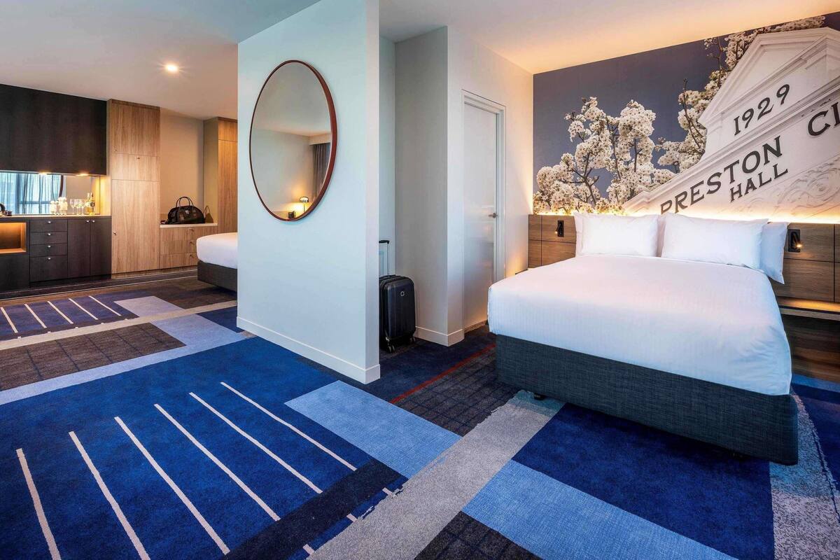 Habitación de hotel con cama, espejo, reloj en la pared, mesita y pared decorada con un diseño floral y el año 1929.