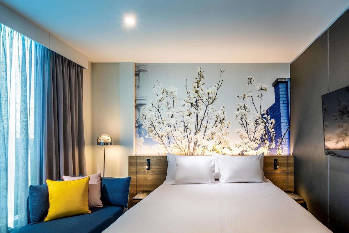 Une chambre d’hôtel avec un grand lit, un canapé agrémenté de coussins colorés, une lampe fixée au mur et un élément décoratif mural.