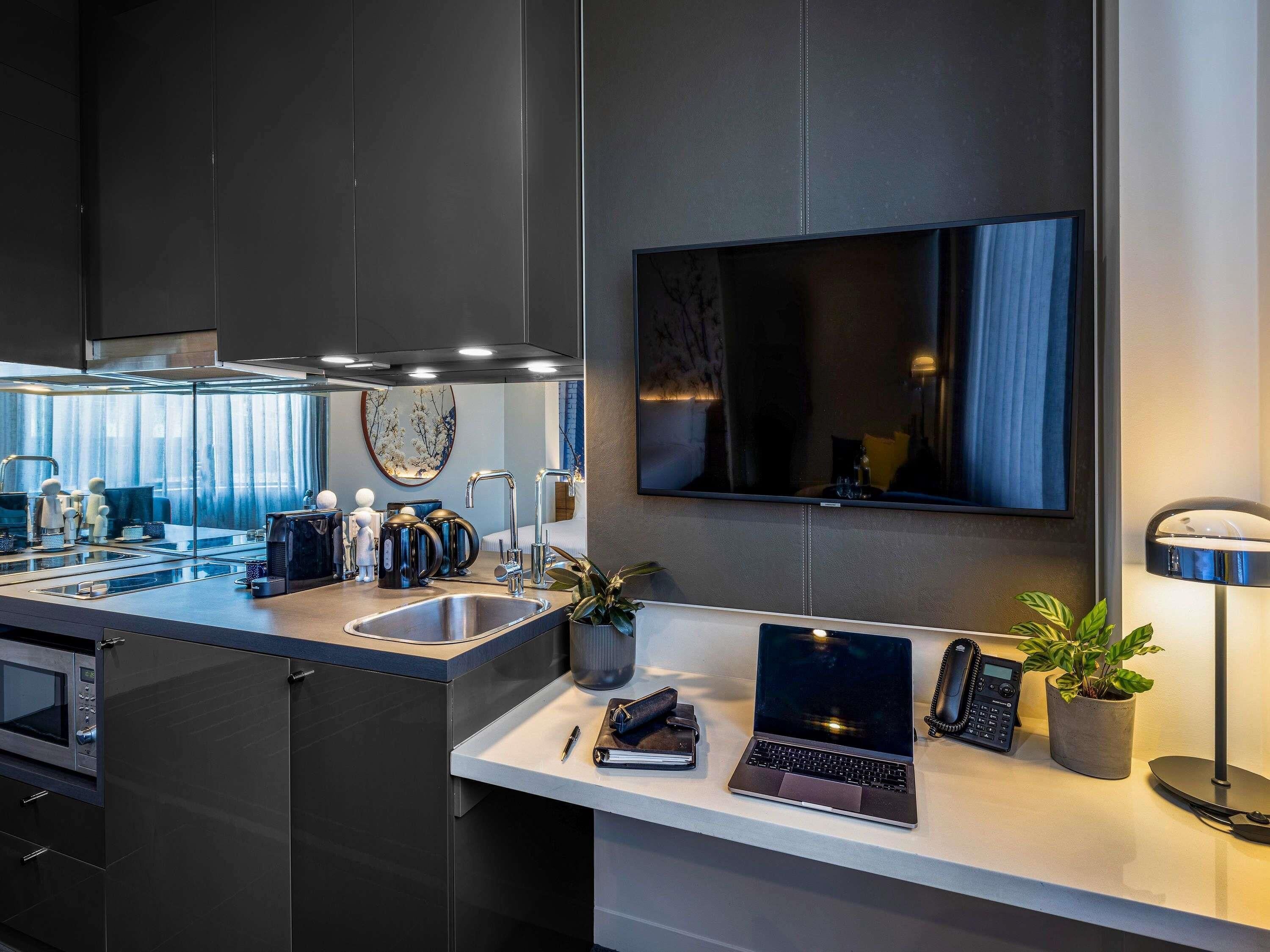 A modern kitchen with a built-in microwave, a sink, and a countertop with a laptop, a phone, and a plant.