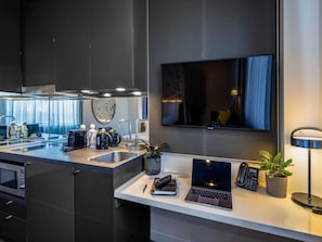 A modern kitchen with a built-in microwave, a sink, and a countertop with a laptop, a phone, and a plant. - Novotel Melbourne Preston (Preston)