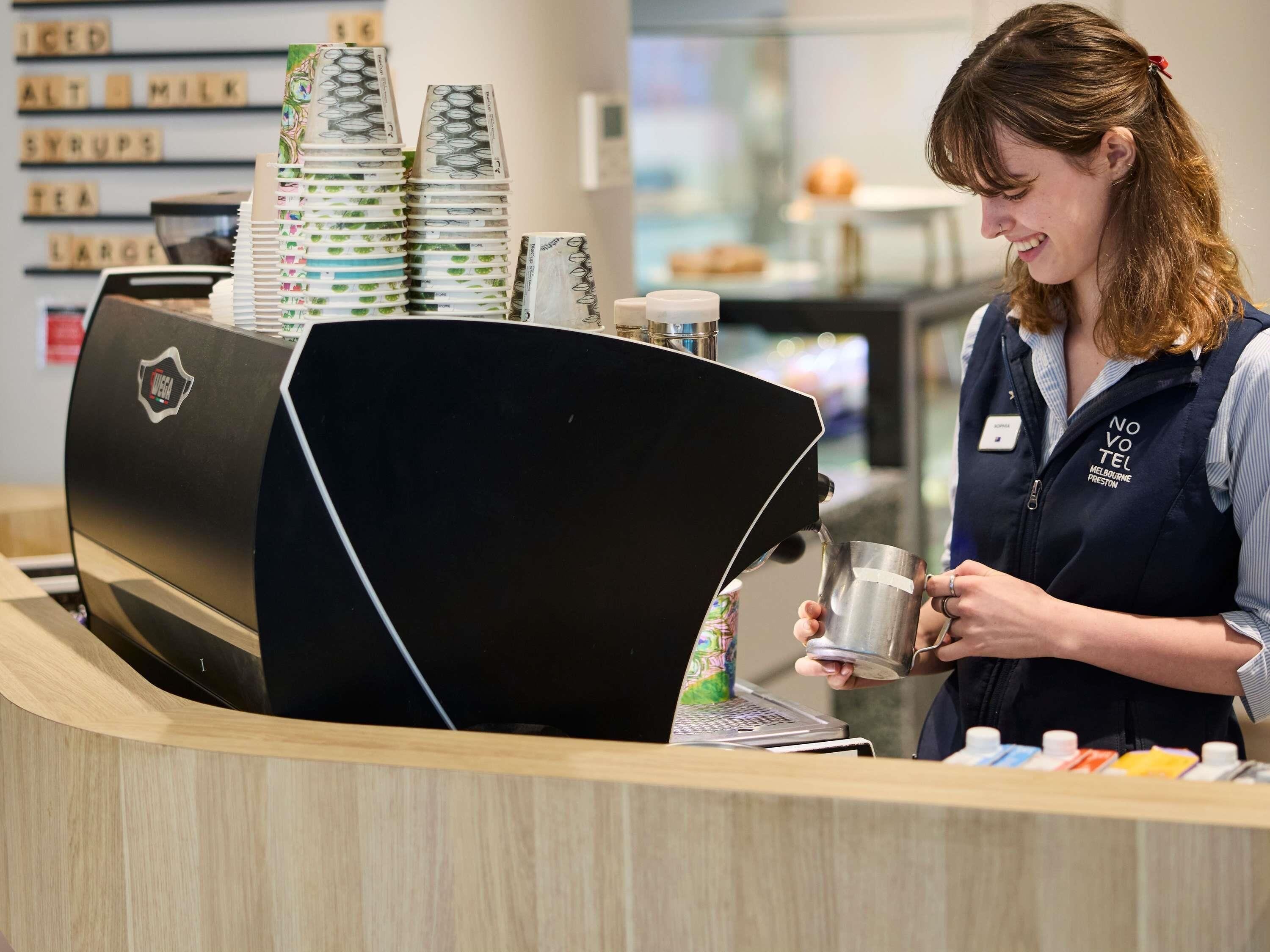 A barista at a coffee shop counter with a coffee machine and stacks of currency notes.