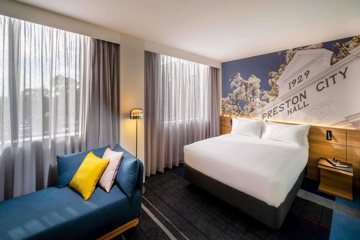 Una habitación de hotel con cama, sofá, lámpara y una pared con el texto '1929 Preston City Hall'.