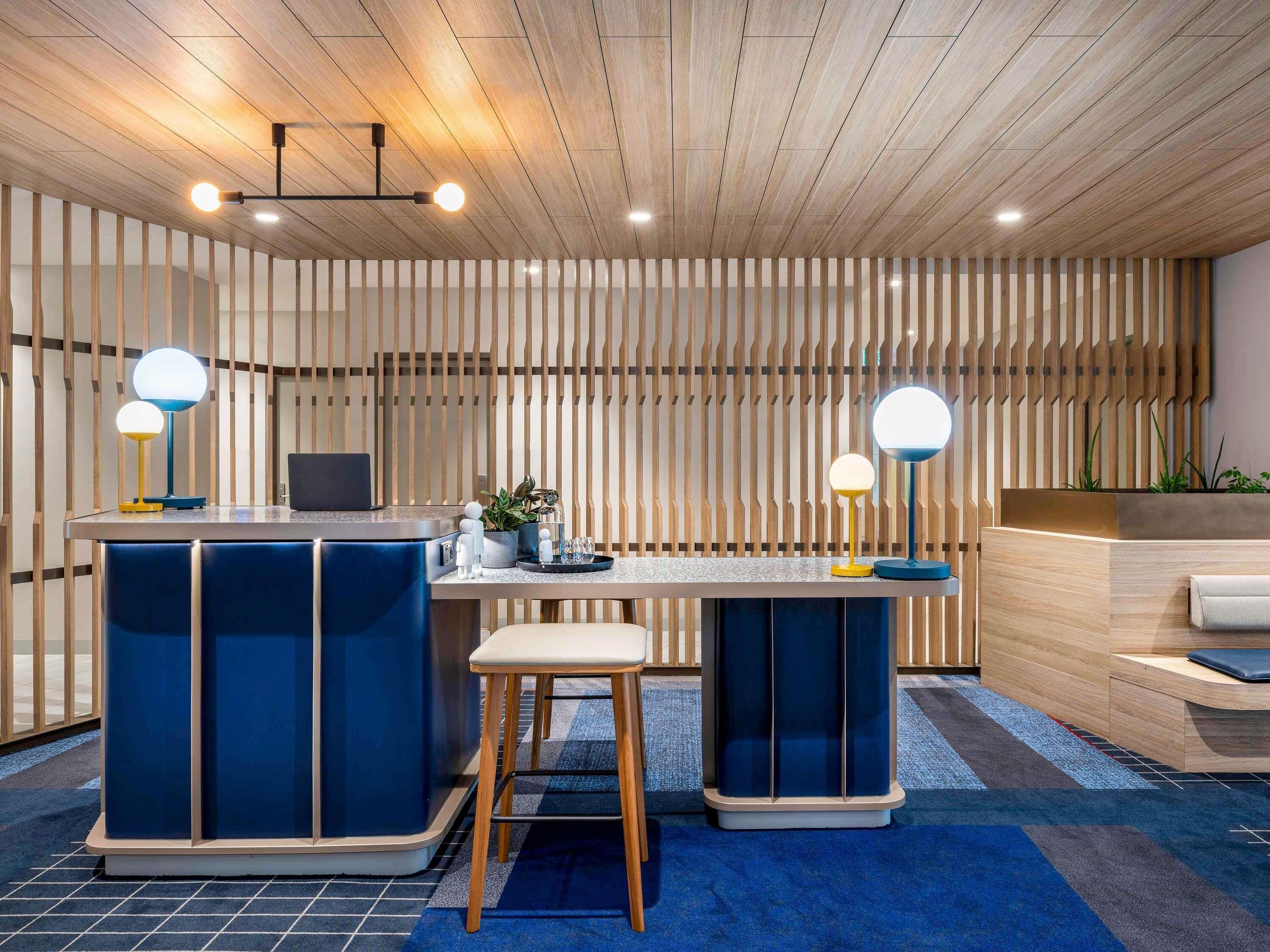 Un espacio de oficina moderno con una pared de listones de madera, un escritorio y dos sillas, y una computadora portátil.