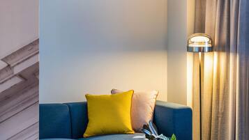 Um sofá azul com almofadas amarelas e castanhas, uma luminária de chão e um vaso com planta.